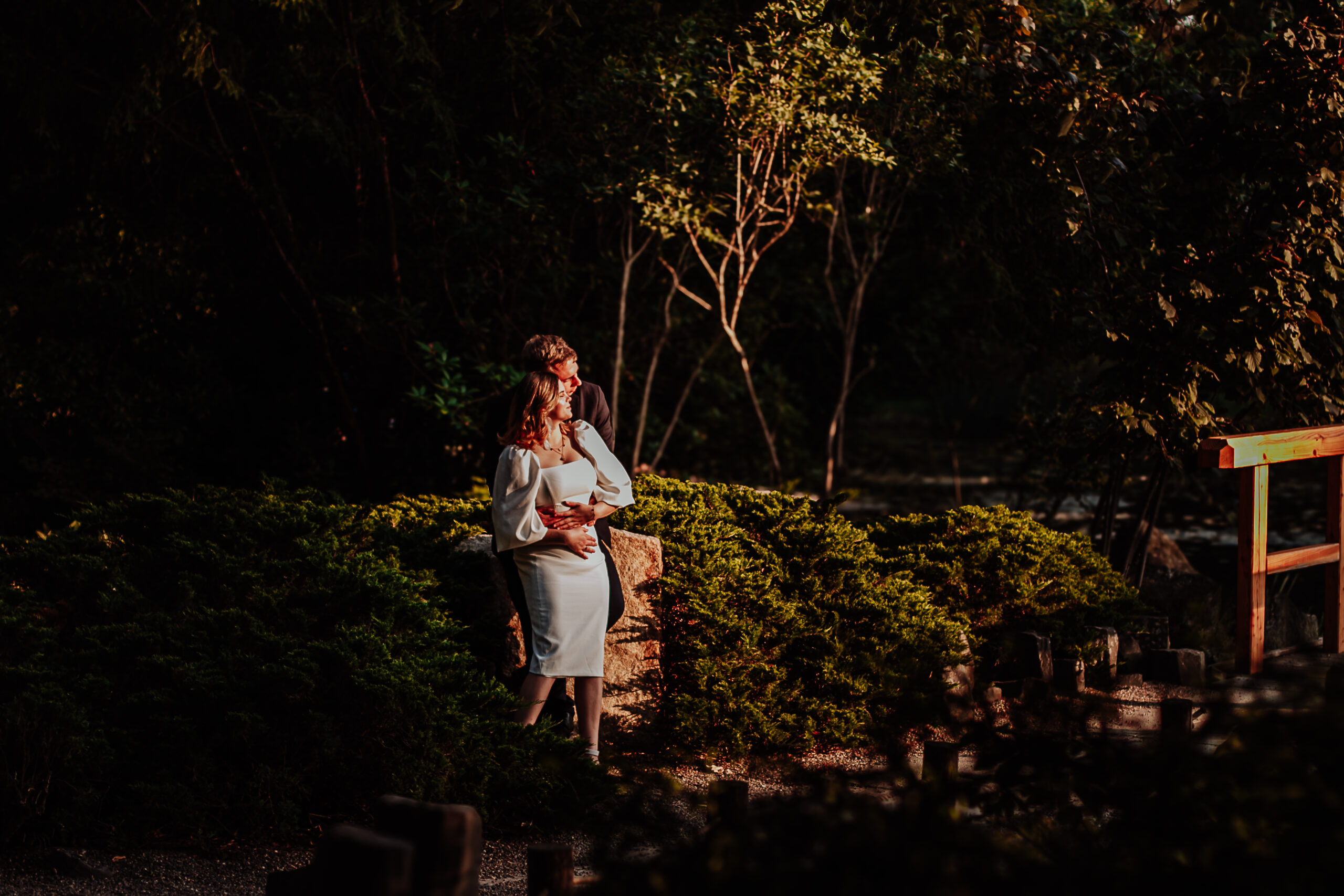 Sesja plenerowa Wrocław – para młoda w eleganckich strojach pozuje w ogrodzie o zachodzie słońca, otoczona zielenią i ciepłym światłem.